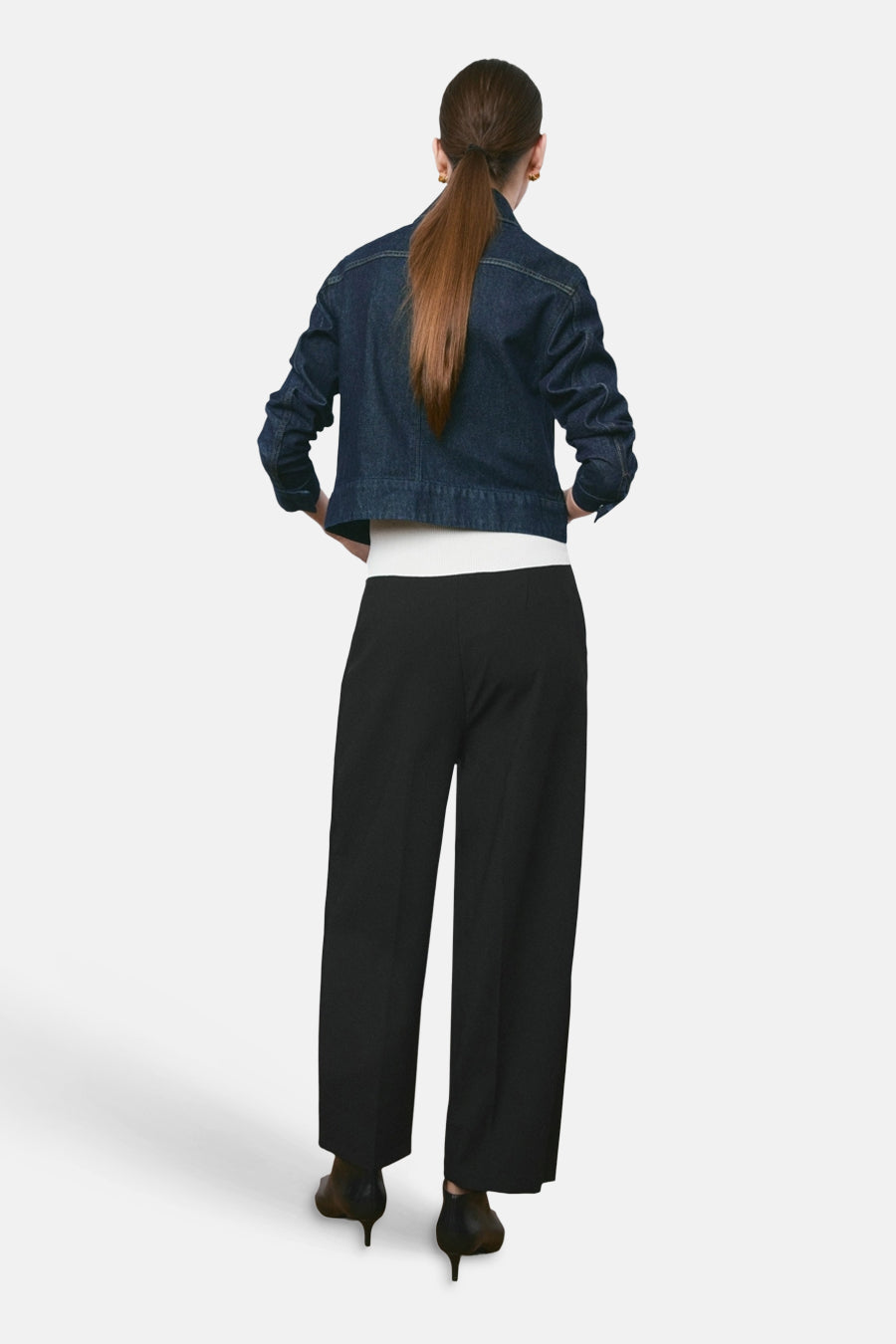 Pantalon noir de MANGO, coupe ample, porté avec une veste en jean courte et des chaussures à talons aiguilles.