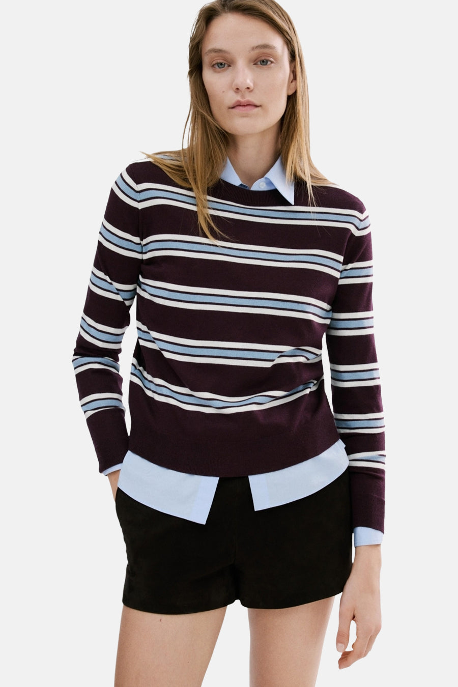 MANGO ronde hals meerkleurige trui, met blauwe en witte horizontale strepen, gedragen over een blauw overhemd en een zwarte korte broek.