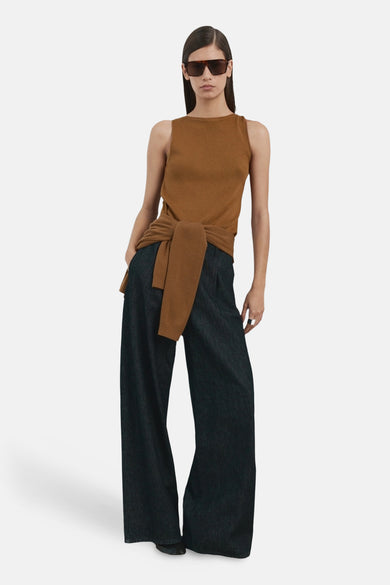 Top sans manches brun par MANGO, noué à la taille, porté avec un pantalon large foncé et des lunettes de soleil.