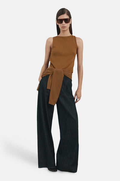 Top sans manches brun par MANGO, noué à la taille, porté avec un pantalon large foncé et des lunettes de soleil.