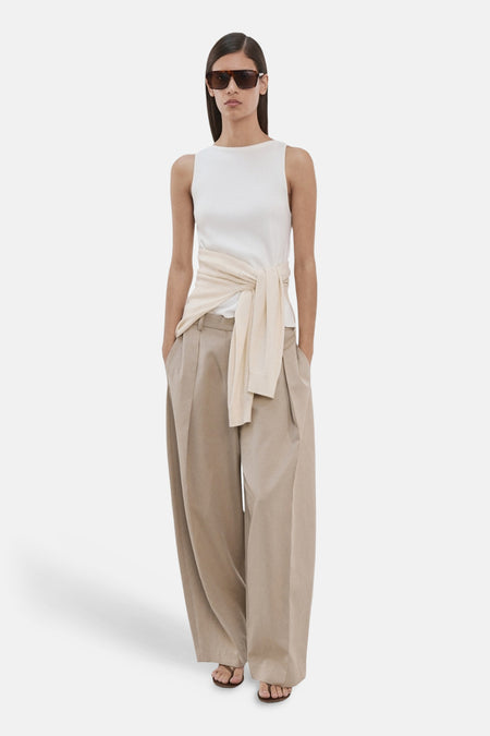 Top écru sans manches de MANGO, porté avec un pull noué et un pantalon taille haute couleur sable.
