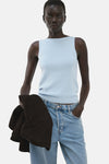 Top bleu sans manches de MANGO porté avec un jean et une veste marron.
