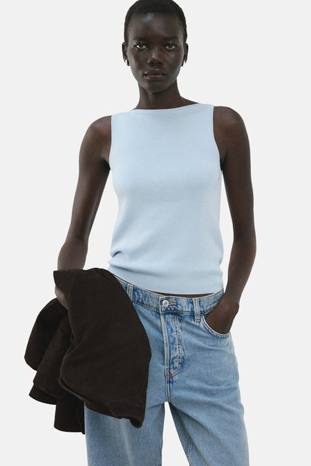 Top bleu sans manches de MANGO porté avec un jean et une veste marron.

