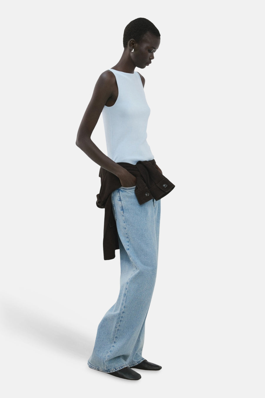 Top sans manches bleu de MANGO, porté avec un jean ample, veste marron à la taille, vue de côté.
