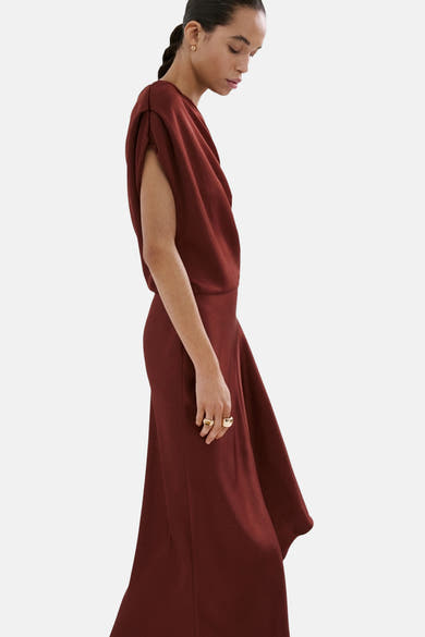 Bordeauxrode jurk van MANGO, asymmetrische snit, gedragen door een model van opzij met gouden sieraden.