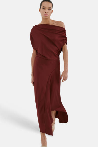 Bordeauxrode jurk van MANGO, gedrapeerd over één schouder, met een asymmetrische split, gedragen met nude pumps.