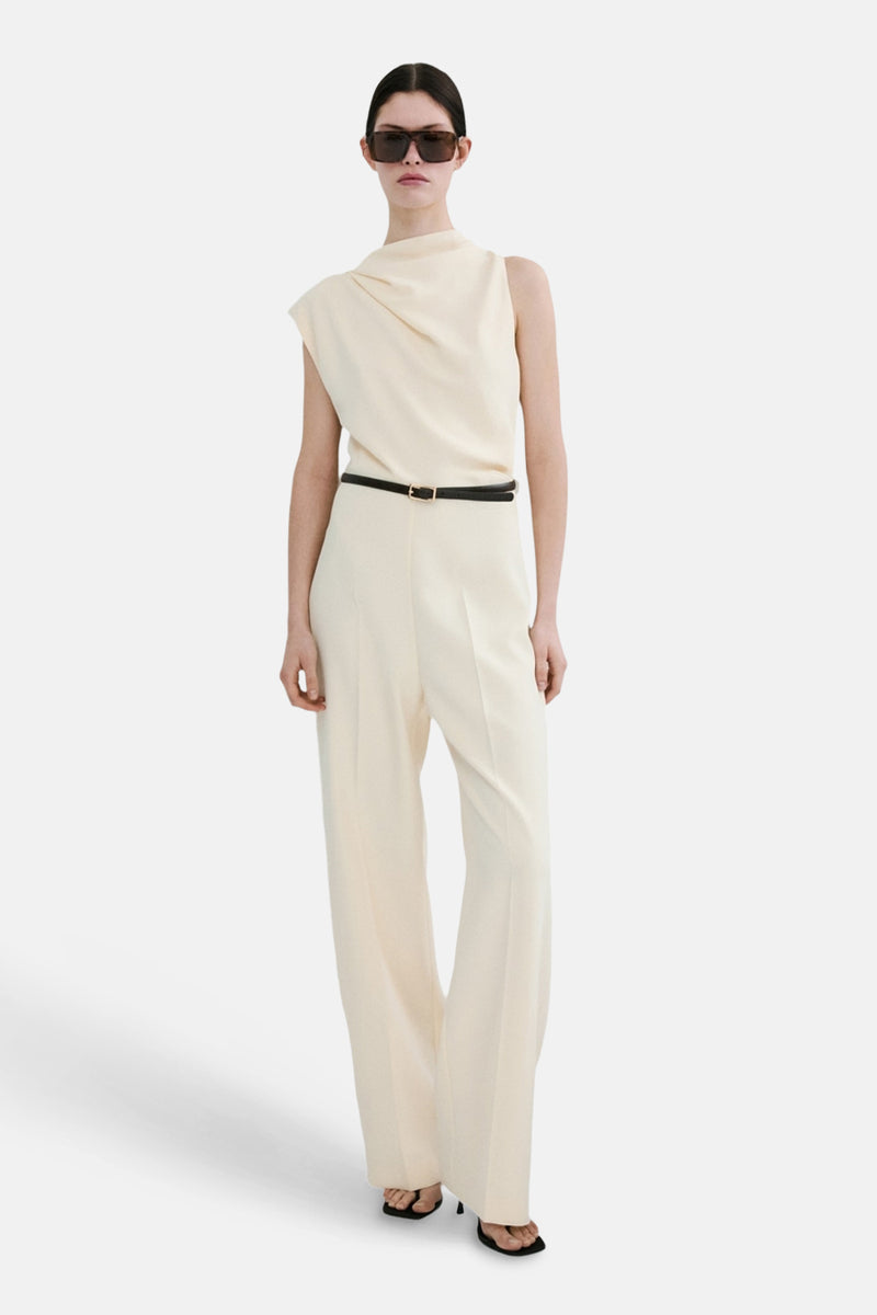 Ecru jumpsuit van MANGO, met een dunne zwarte riem met gouden gesp, gedragen over de kleding.