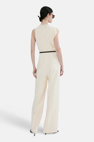 Ecru jumpsuit van MANGO, met dunne zwarte riem en wijde pijpen, van achteren gezien.