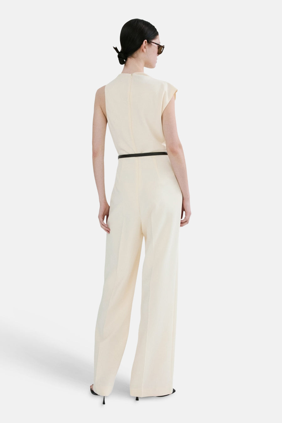 Ecru jumpsuit van MANGO, met dunne zwarte riem en wijde pijpen, van achteren gezien.