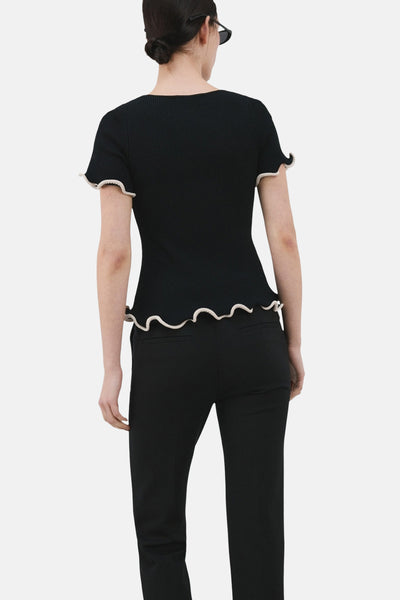 Pull col rond noir de MANGO, orné de volants contrastants à l'encolure et aux manches, porté avec un pantalon noir.