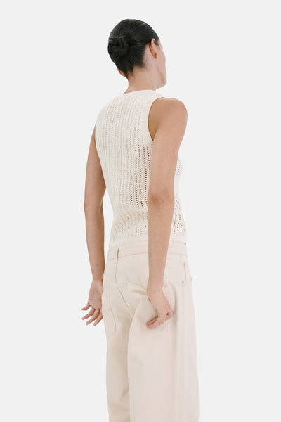 Top sans manches écru de MANGO, en maille ajourée, porté de dos avec un pantalon large beige.