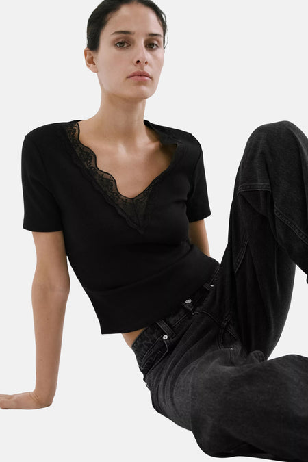 Effaatzwart T-shirt met korte mouwen van MANGO, in ribgebreide stof, van achteren gezien met een donkergrijze jeans.