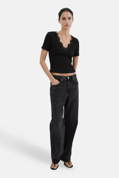 Zwart geribd T-shirt met V-hals en kanten afwerking van MANGO, korte mouwen en een korte pasvorm, gedragen met een wijde zwarte jeans en teenslippers.