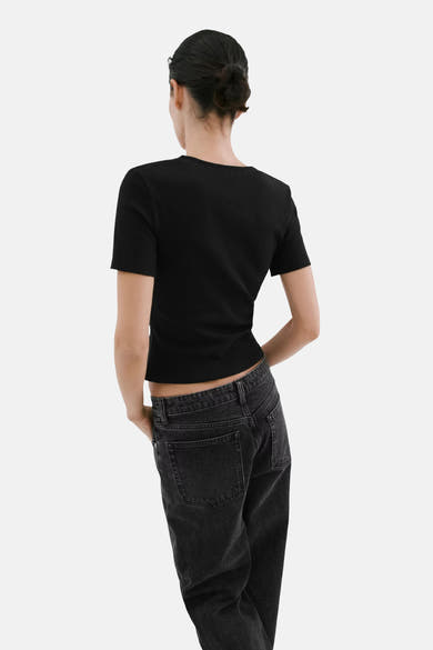 T-shirt noir uni à manches courtes de MANGO, en maille côtelée, vu de dos avec un jean gris foncé.