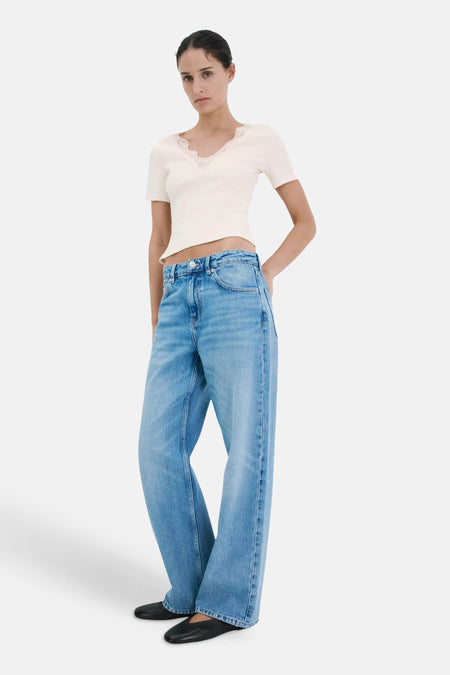 T-shirt écru côtelé de MANGO, col en V en dentelle, manches courtes, porté avec un jean large et des chaussures plates noires.