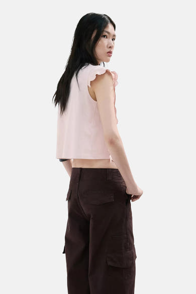 Blouse sans manches rose de MANGO à volants en dentelle, coupe courte, portée avec un pantalon cargo marron.
