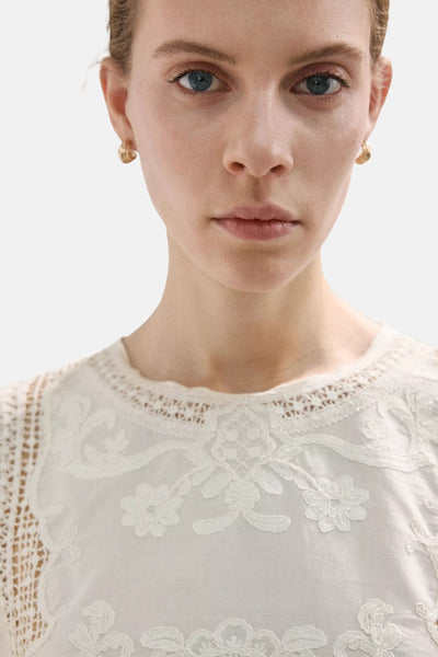 Blouse beige de MANGO à broderie florale et bordure en crochet au col, portée par une femme.