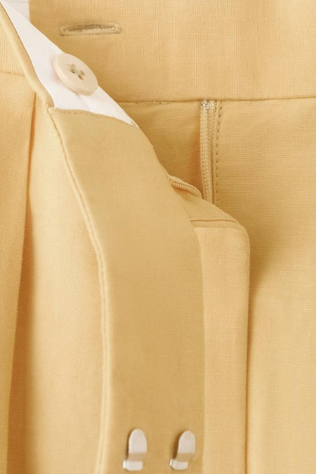 Pantalon jaune de MANGO, avec fermeture éclair et bouton, détails de plis et passants de ceinture.
