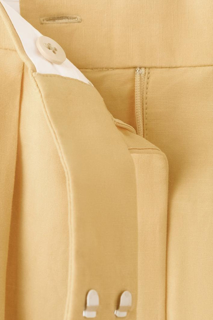 Pantalon jaune de MANGO, avec fermeture éclair et bouton, détails de plis et passants de ceinture.
