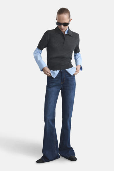 Donkerblauwe flared jeans van MANGO, gedragen met een lichtblauw overhemd en een grijze polo.