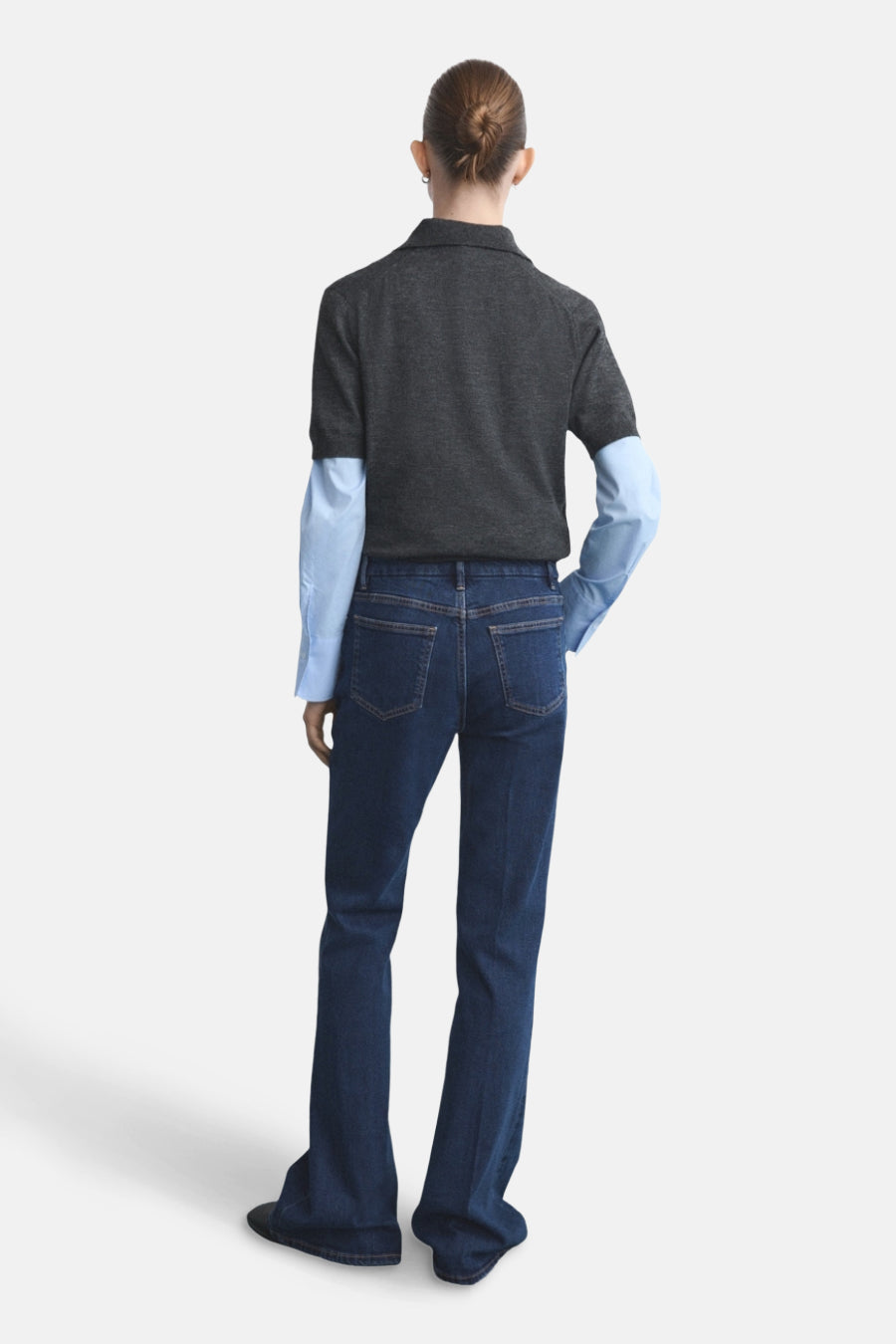 Jean évasé bleu foncé de MANGO, vue arrière, porté avec un chemisier bleu clair et un pull gris.
