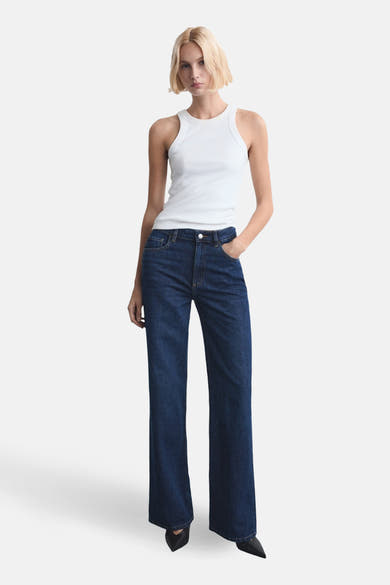 Jean droit en denim bleu foncé de MANGO, porté avec un débardeur blanc et des chaussures pointues noires.