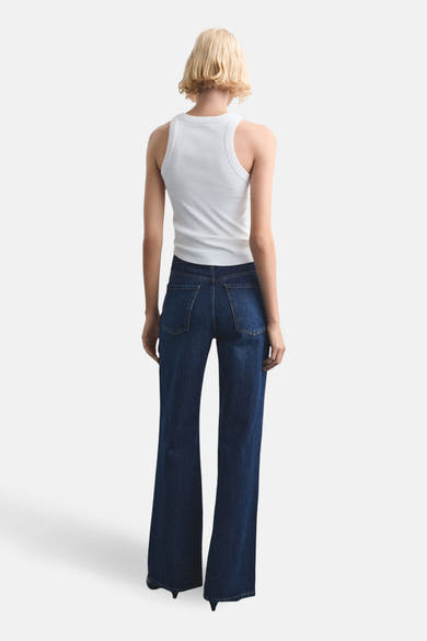 Jean droit en denim bleu foncé de MANGO, avec une coupe ample, porté avec un débardeur blanc.