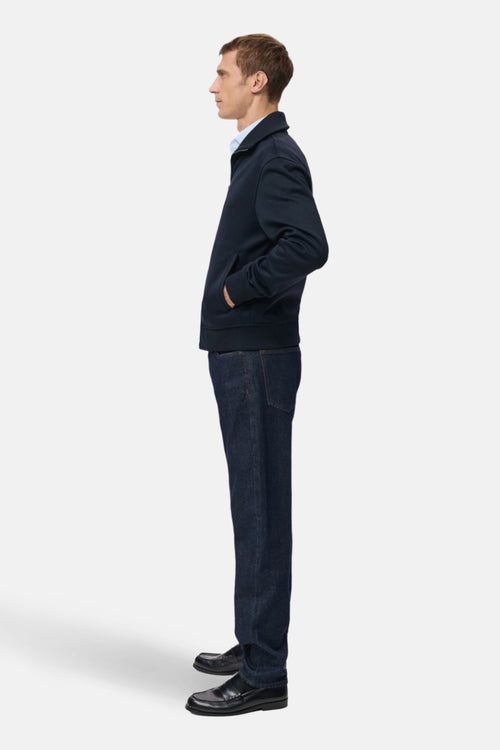 Sweat bleu de MANGO, porté avec un pantalon en denim foncé et des mocassins noirs, vue de profil.
