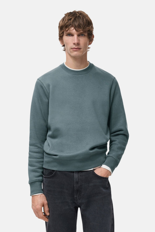 Sweat bleu de MANGO, porté avec un jean noir et un t-shirt blanc, manches longues, col rond.