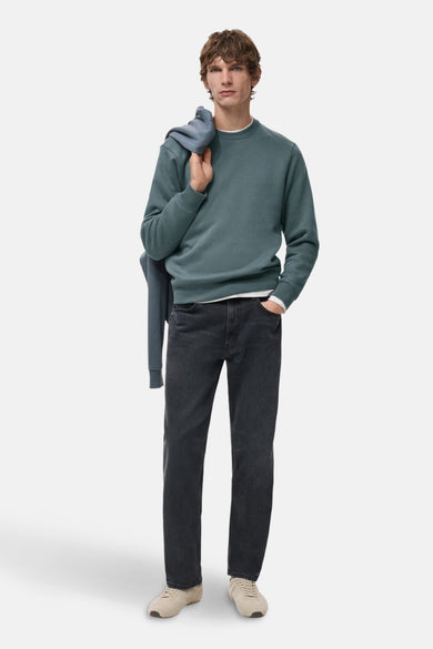Sweat bleu de MANGO avec un autre sweat sur l'épaule, porté avec un jean noir et des baskets.