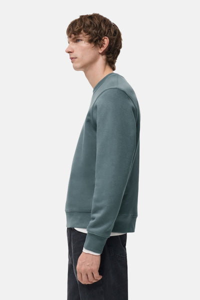 Blauwe MANGO-sweatshirt, van opzij gezien, gedragen met een wit T-shirt en een donkere broek.