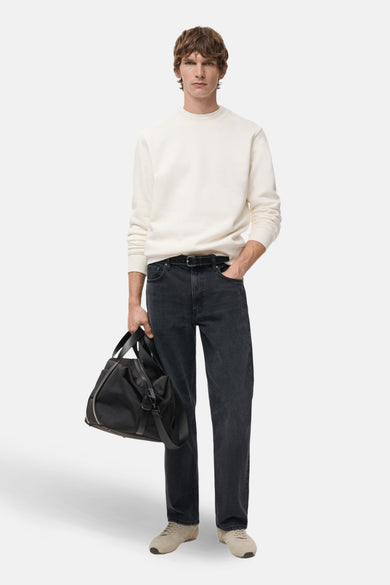 Witte rondehals sweatshirt van MANGO, gedragen met een spijkerbroek en casual schoenen, met een zwarte reistas in de hand.