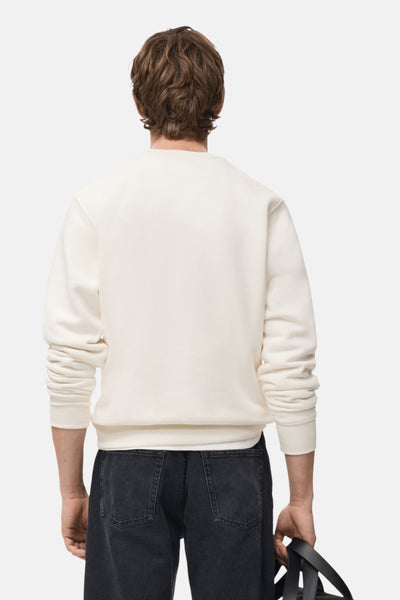 Sweat-shirt blanc de MANGO, vu de dos, porté avec un jean noir et tenant un sac noir.
