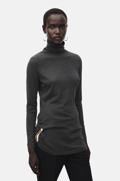 Grijze rondehals trui van MANGO, met ritssluitingdetails en gedragen met een zwarte broek.
