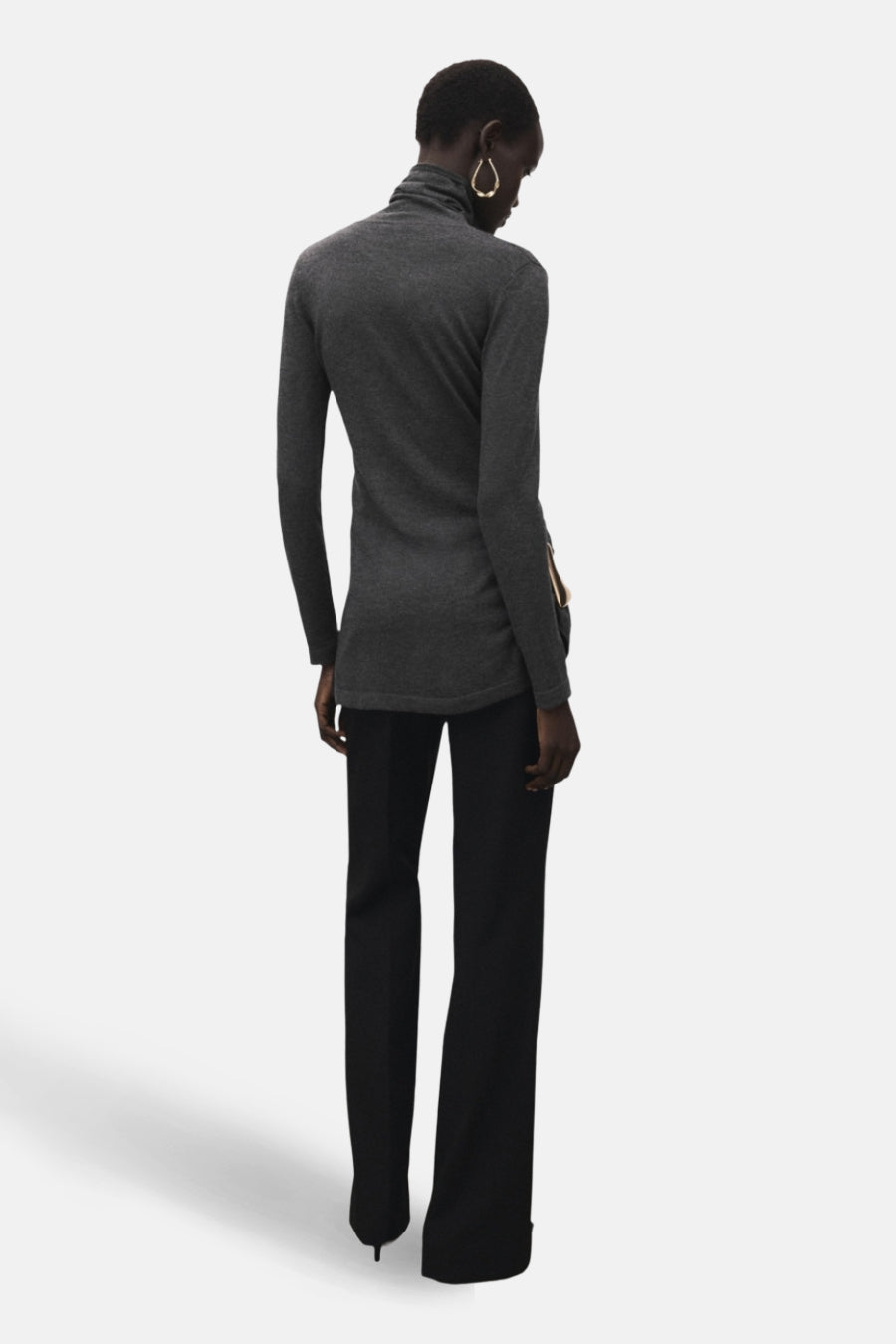 Pull à col rond gris de MANGO, avec des détails de fermeture éclair et porté avec un pantalon noir.