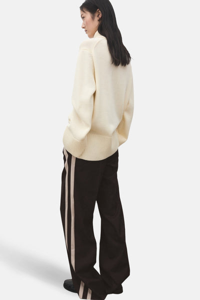 Pantalon marron avec rayures crème de MANGO, porté avec un pull en laine, vue de dos.
