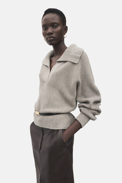 Beige V-hals trui van MANGO, met een bruine leren rok en gouden oorbellen.