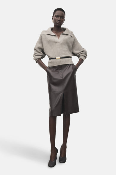 Beige V-hals trui van MANGO, gedragen met een bruine leren rok en een zwarte riem.