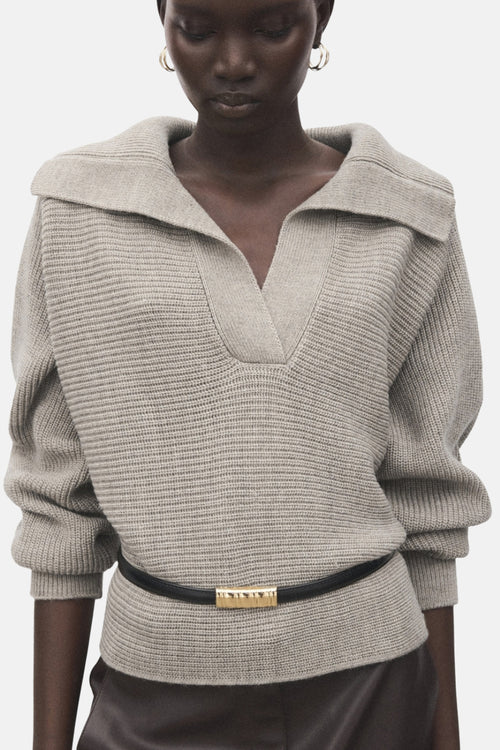 Pull à col en V beige de MANGO, agrémenté d'une ceinture noire avec une boucle dorée.