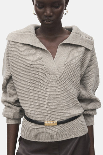Beige V-hals trui van MANGO, versierd met een zwarte riem met een gouden gesp.