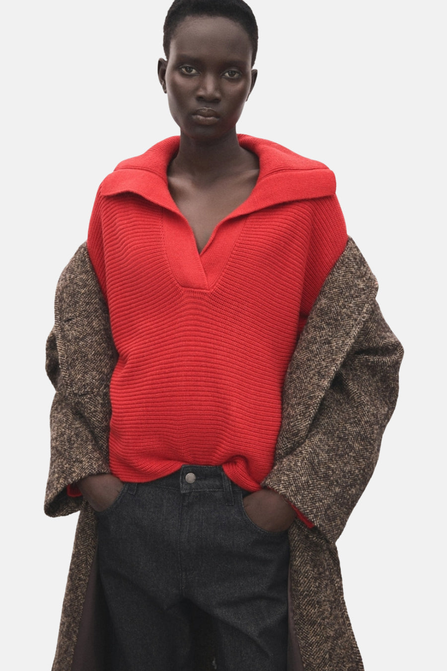 Pull à col en V rouge de MANGO, porté avec une veste à chevrons et un jean délavé.