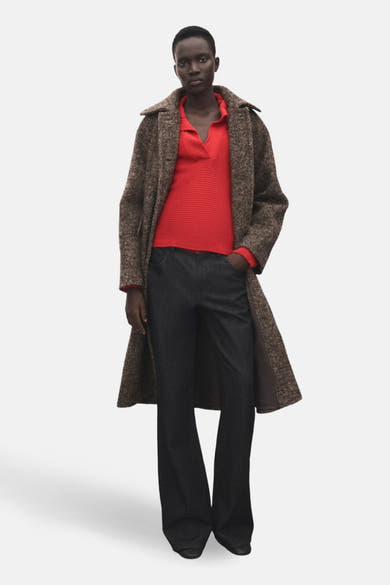 Pull à col en V rouge de MANGO, à fines côtes horizontales, porté avec un manteau long marron.