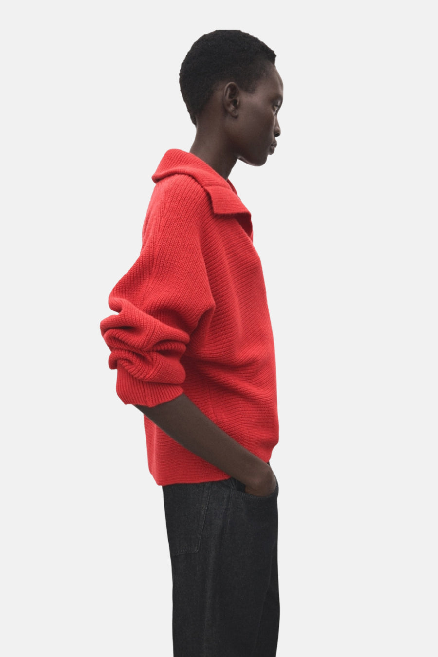 Pull à col en V rouge de MANGO, manches longues avec plis décoratifs, porté avec un pantalon en denim sombre, vue de côté.