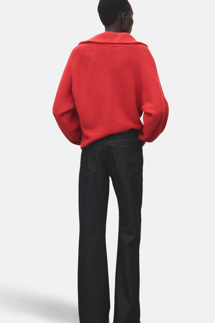 Pull à col en V rouge de MANGO, en maille côtelée, porté avec un jean noir à jambes évasées.