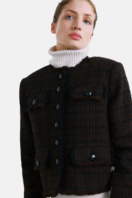 Veste brune de MANGO, à carreaux, avec des poches à rabat et une bordure effilochée, portée sur un col roulé blanc.
