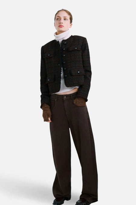 Veste marron par MANGO avec des poches, portée avec un pull col roulé blanc et un pantalon marron ample.