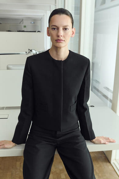 Blazer noir de MANGO avec une coupe courte et des poches discrètes, porté avec un pantalon noir assorti.