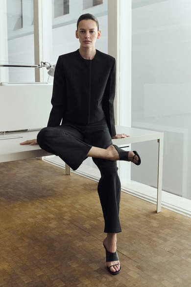 Blazer noir de MANGO, porté avec un pantalon noir ample et des mules à talons bas.