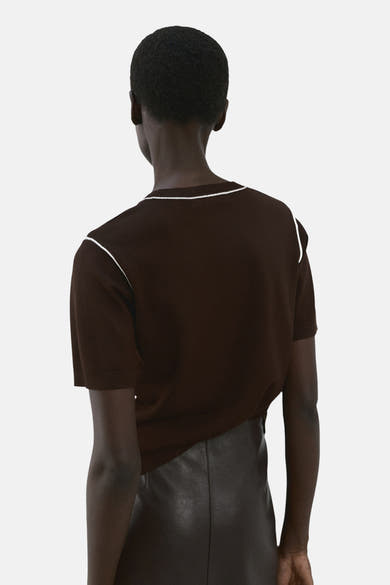 Pull à col rond brun de MANGO, avec bordure blanche au col et aux épaules, porté avec une jupe en cuir marron.
