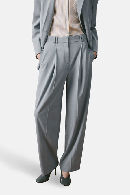 Pantalon de costume bleu van MANGO, coupe ample avec des plis, porté avec une chemise rayée et un veston assorti.